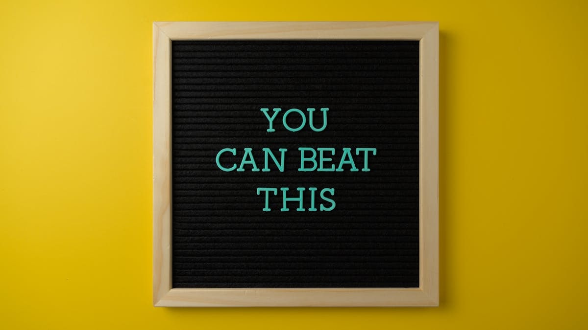 Black letter board with motivational phrase 'You Can Beat This' on vibrant yellow background.