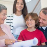 Smiling family indoors signing real estate documents. Friendly interaction and teamwork.